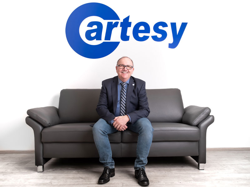 Cartesy employee on couch with blue Cartesy logo in the background